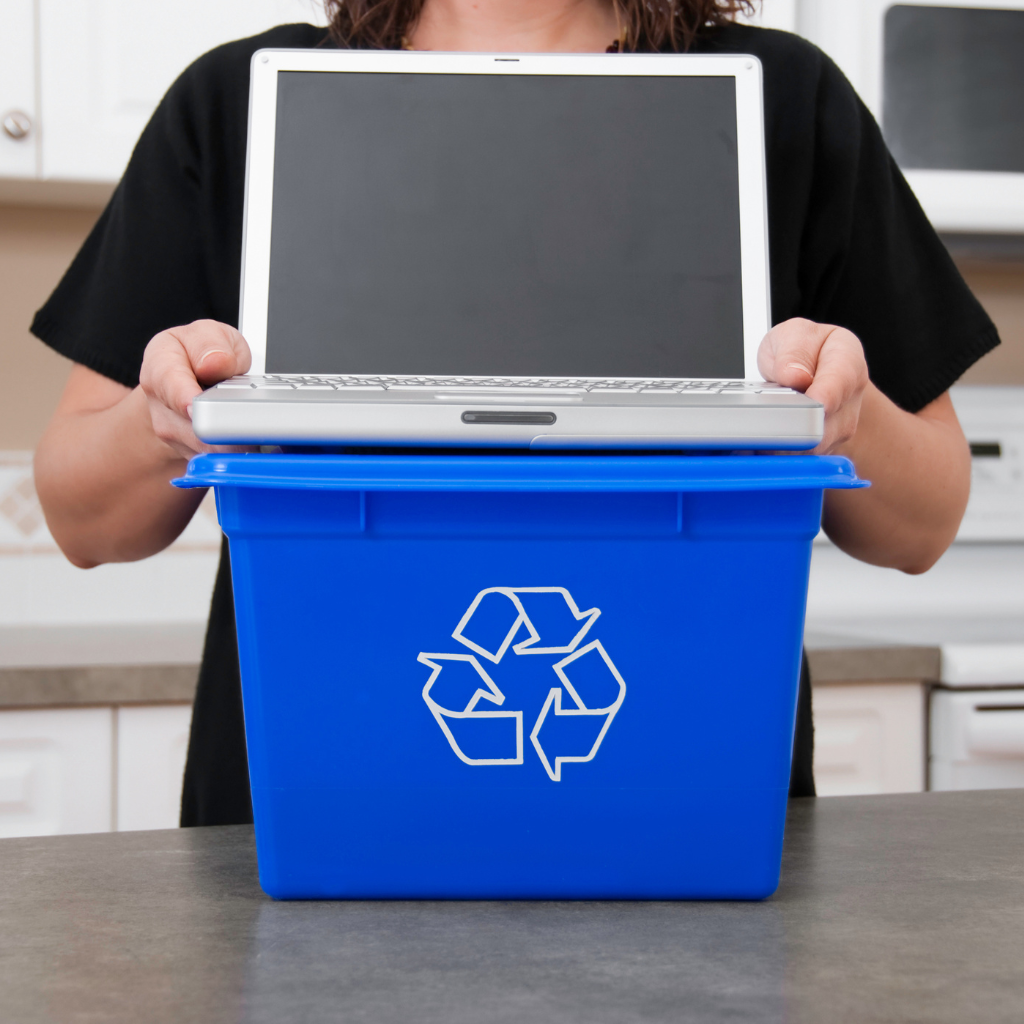 Laptop held by a person above a blue recycling bin on a table