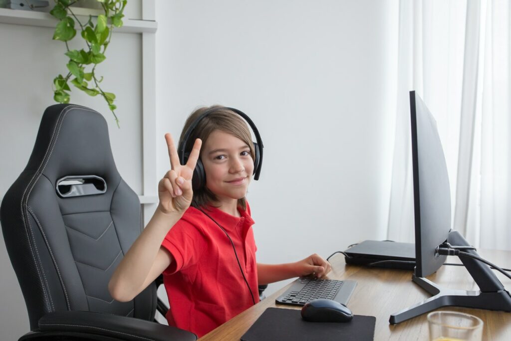 Child sitting at a computer holding up peace sign.